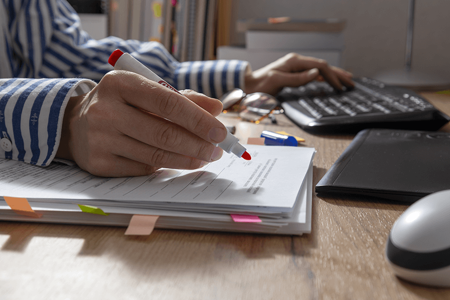 Closeup of woman hand who holding red marker and cheking text for grammar and using computer