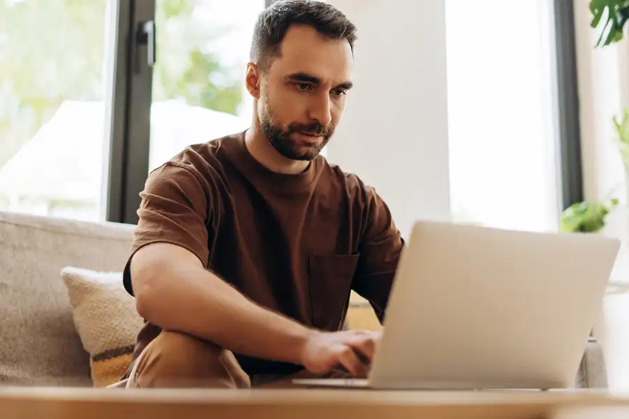 Middle-aged man sitting on his couch in is living room working on his laptop.